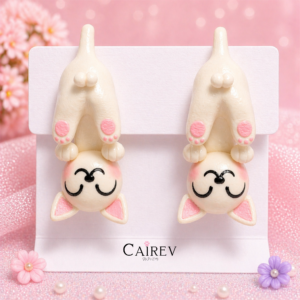 Aretes de gatito blanco de cabeza abajo hechos a mano con detalles rosas sobre fondo pastel