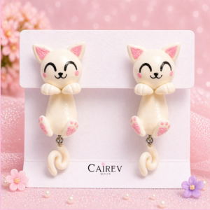 Aretes de gatito blanco sonriente hechos a mano con cola colgante y detalles rosas sobre fondo pastel