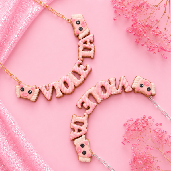 Collares personalizados de cerdito con alas kawaii con nombres decorados en rosa, uno con cadena dorada y otro con cadena plateada.