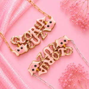 Collares personalizados de cerdito con alas kawaii con nombres decorados en rosa, uno con cadena dorada y otro con cadena plateada.
