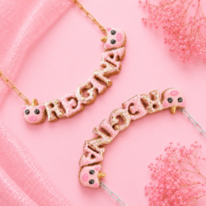 Collares personalizados de cerdito unicornio kawaii con nombres decorados, uno con cadena dorada y otro con cadena plateada.
