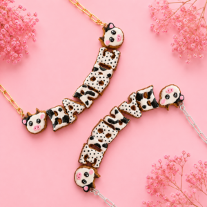 Collares personalizados de vaquita kawaii con nombres decorados, uno con cadena dorada y otro con cadena plateada.